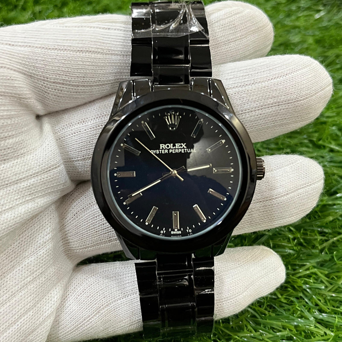 Black watch held in a white glove on green grass